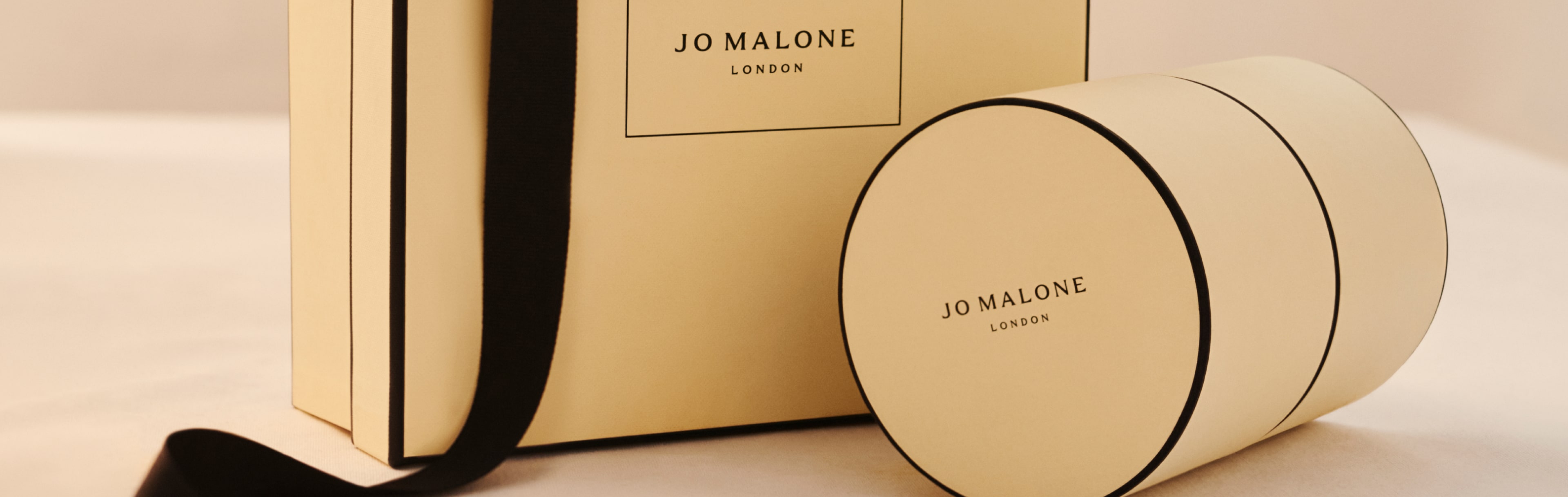 woman sitting on a hill, holding classic jo malone london black and cream gift boxes